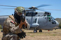 a soldier with a gun in front of a helicopter